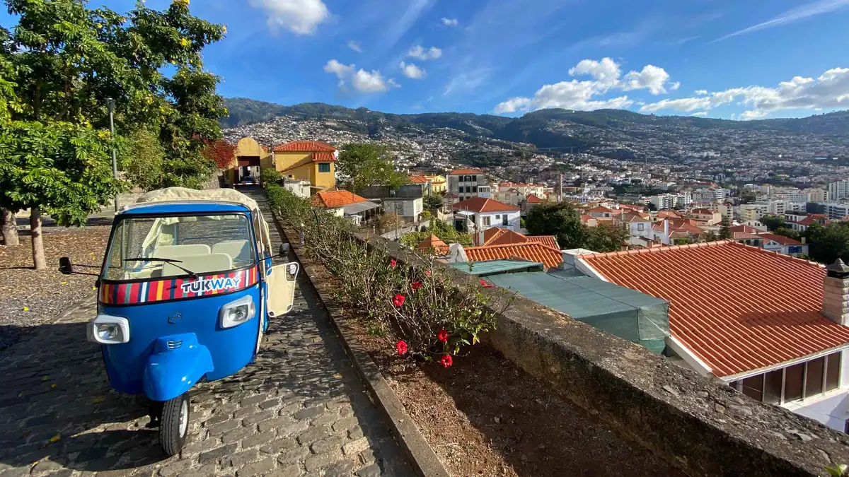 A tuk-tuk parked at a hilltop viewpoint over Funchal Bay on a City Highlights Tuk-Tuk Tour in Funchal, Portugal