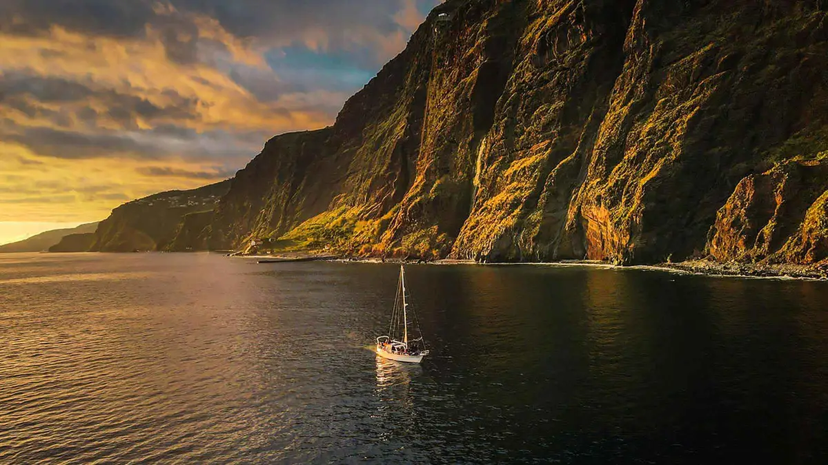 A sailing boat anchored near Cabo Girão at sunset with passengers snorkeling on a Funchal sunset sailing tour in Funchal, Portugal