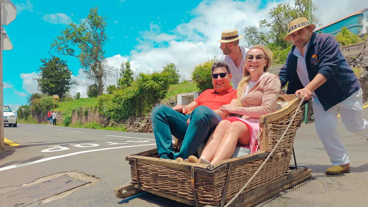 Two toboggan runners steering a wicker basket sledge down a paved street from Monte on a Funchal Monte toboggan tour by tuk-tuk in Monte, Madeira